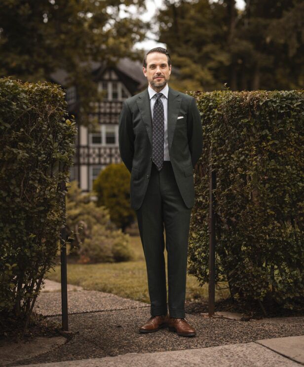 Forest green flannel suit with striped shirt, medallion tie and brown derbies, worn by a model in a garden