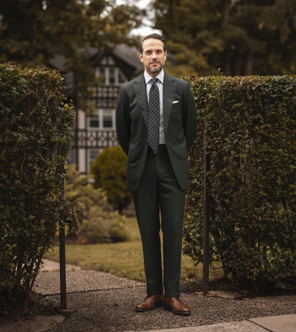 Forest green flannel suit with striped shirt, medallion tie and brown derbies, worn by a model in a garden