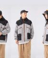 Grey and black colourblock hooded nylon jacket with orange zips, styled with tan trousers, worn by a model in three views