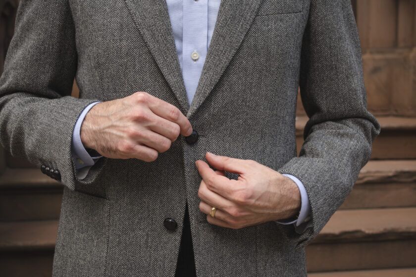 Grey herringbone tweed sport coat with leather buttons and blue oxford shirt, close-up of the button being fastened