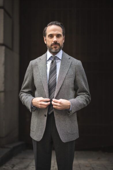 Grey herringbone tweed sport coat with blue shirt, striped tie and charcoal flannel trousers, worn by a model