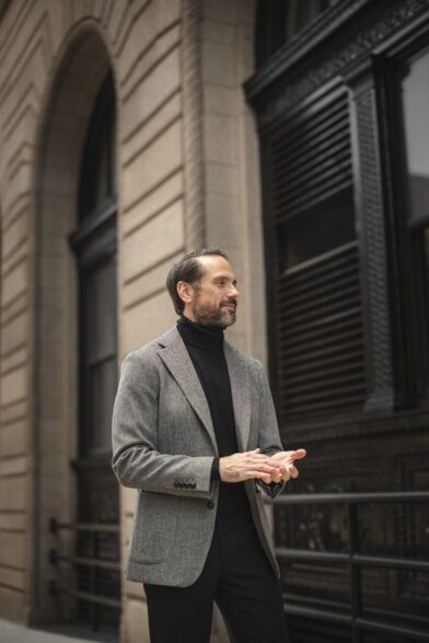 Grey herringbone tweed sport coat with black turtleneck and black trousers, worn by a model on a city street