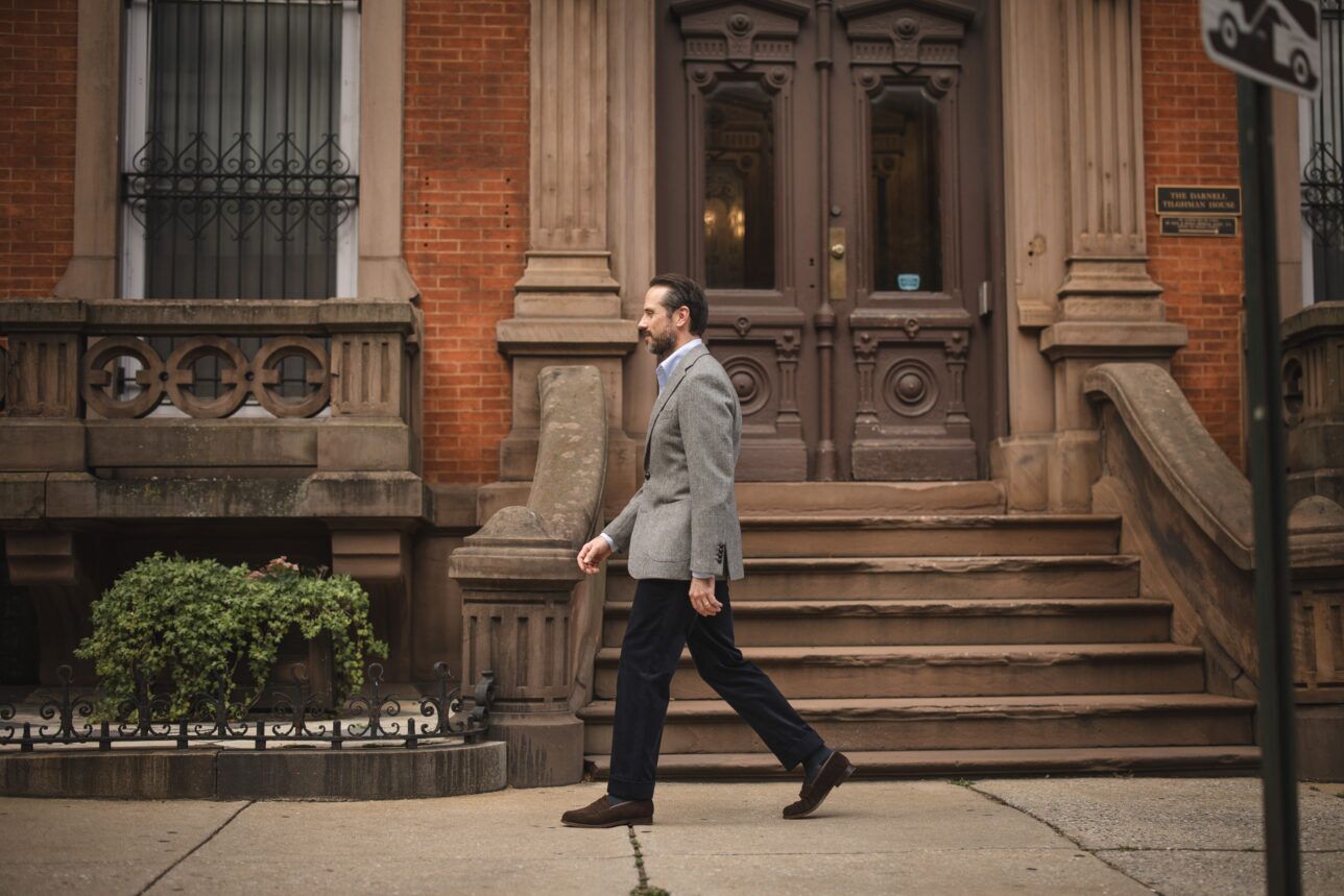 Grey tweed sport coat with blue shirt, navy corduroy trousers and brown suede loafers, worn by a model on a brownstone street