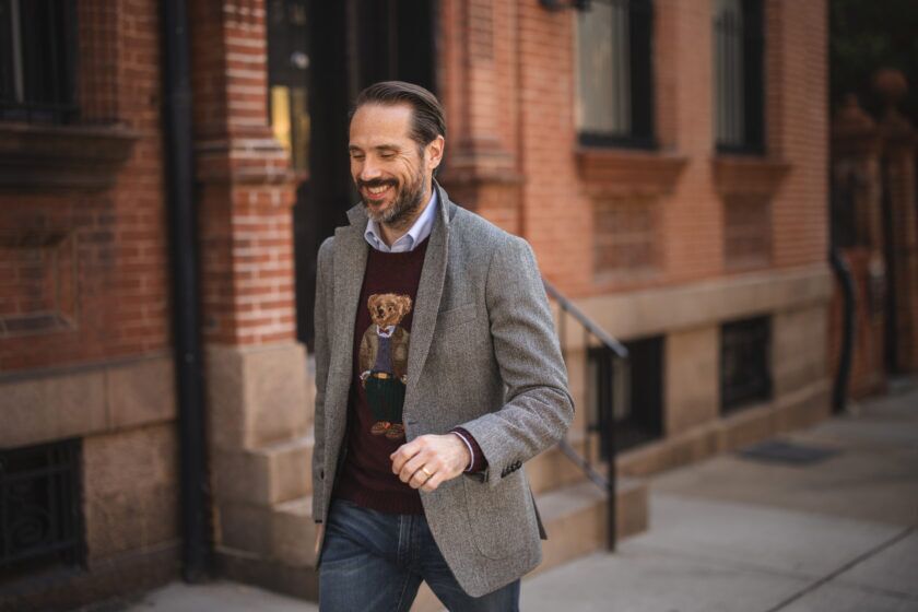 Grey herringbone tweed sport coat with a burgundy bear intarsia sweater and jeans, on a brick street