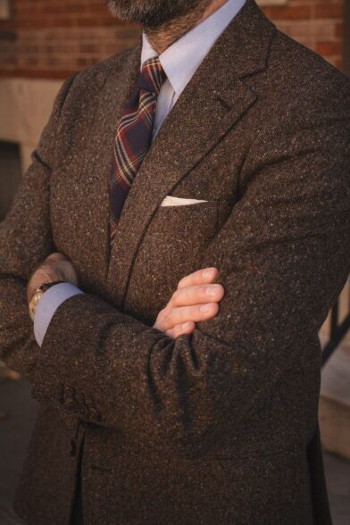 Brown donegal tweed suit jacket with blue shirt, plaid wool tie and white pocket square, worn by a model