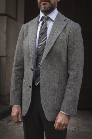 Grey herringbone tweed sport coat with light blue shirt, striped tie and charcoal flannel trousers, worn by a model