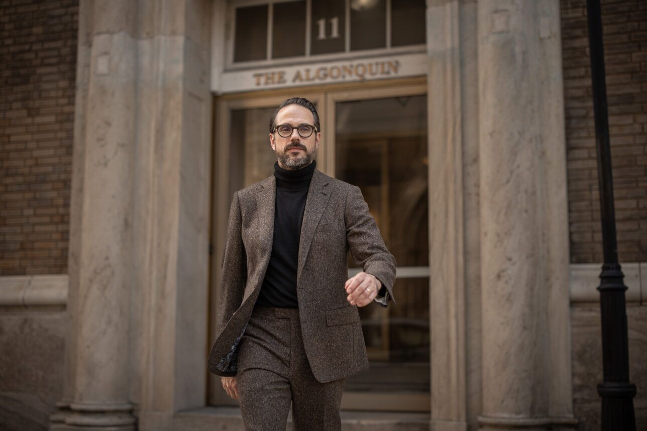 Brown donegal tweed suit with black turtleneck, worn by a model outside a hotel entrance