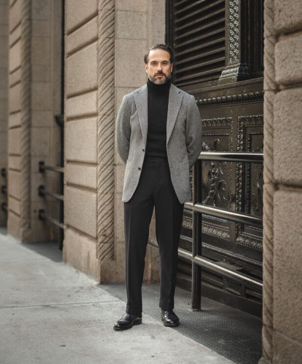 Grey tweed sport coat with black turtleneck, black trousers and black loafers, worn by a model on a city street