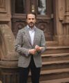 Gray herringbone tweed sport coat with light blue shirt and navy trousers, worn by a model on brownstone steps