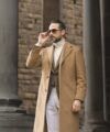 Camel wool overcoat with brown checked waistcoat, cream turtleneck and white trousers, worn by a model on a colonnaded street