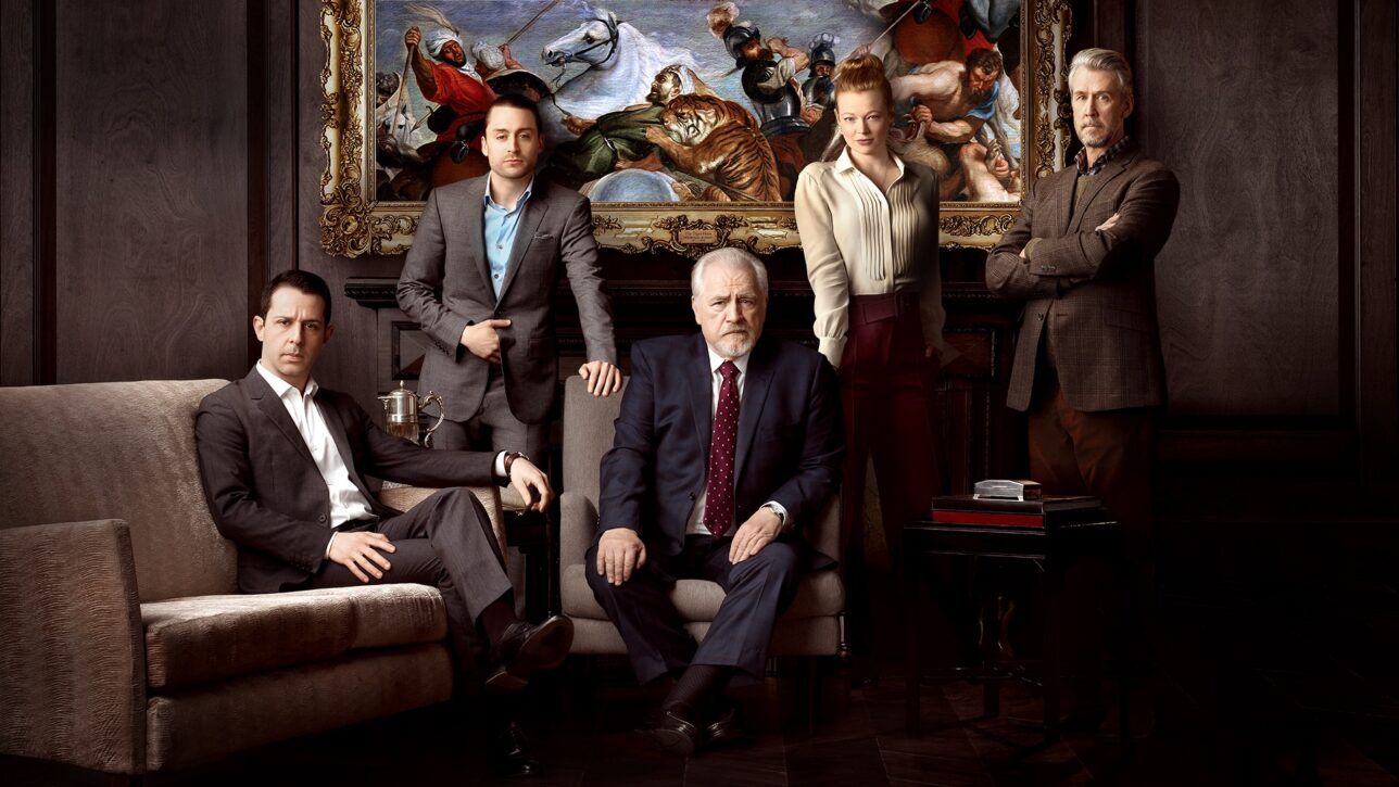 Navy suit with white shirt and burgundy dotted tie among grey suits and a brown tweed jacket, styled group scene