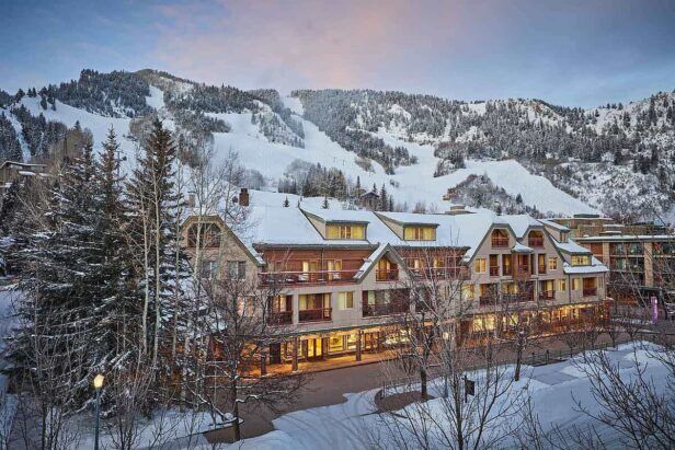 Snow-covered mountain lodge hotel lit at dusk below ski slopes and pines, a winter lifestyle scene