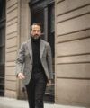 Grey tweed sport coat with black turtleneck and black trousers, worn by a model on a city street