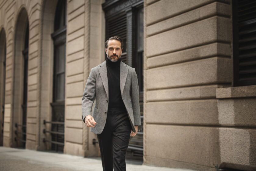 Grey tweed sport coat with black turtleneck and black trousers, worn by a model on a city street
