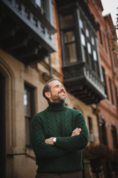 Forest green cable knit turtleneck sweater with brown tweed trousers, worn by a model on a city street