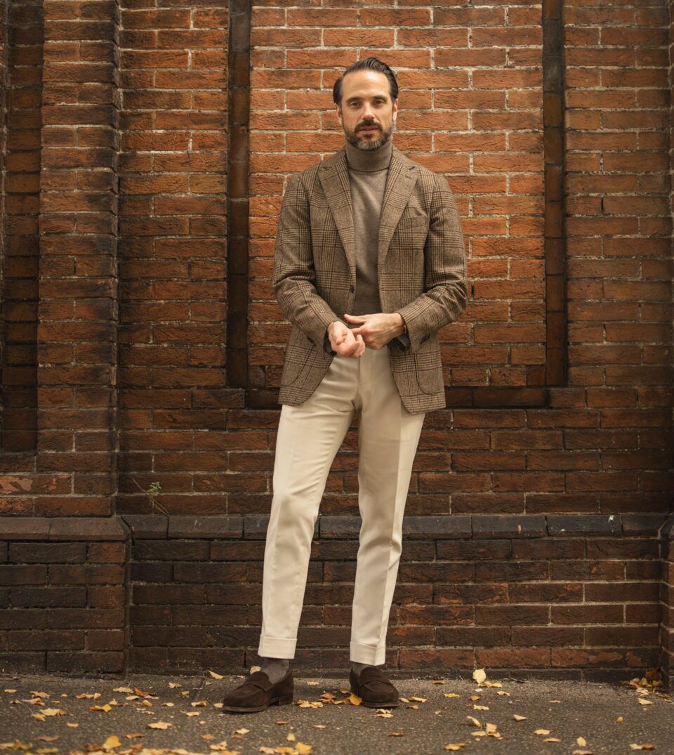 Brown glen plaid wool sport coat with taupe turtleneck, cream trousers and brown suede loafers, worn by a model