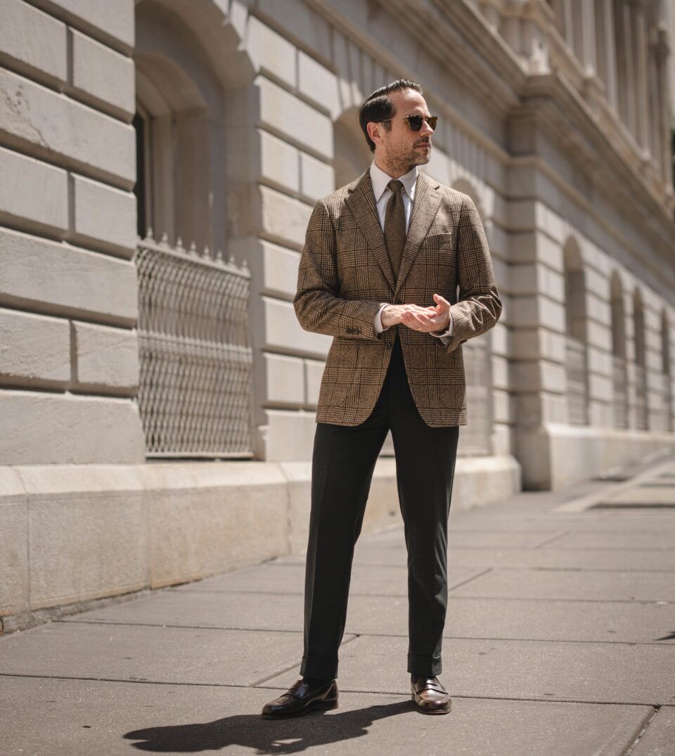 Brown glen check wool sport coat with white shirt, olive tie and dark green trousers, worn by a model on a city street