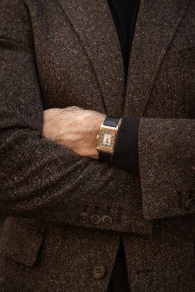 Brown flecked donegal tweed jacket with black turtleneck and rose gold rectangular watch, a close-up detail