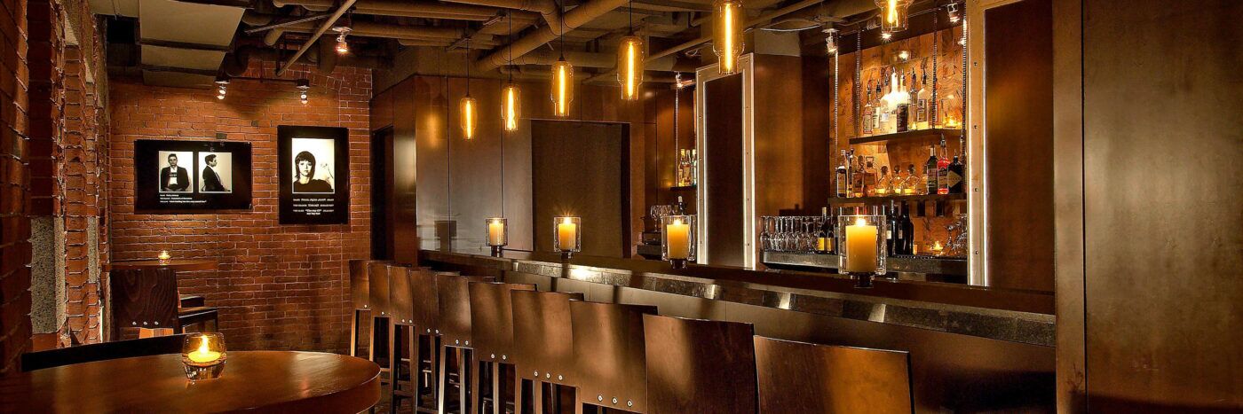 Dimly lit bar interior with exposed brick, candlelit counter and wooden stools, a styled lifestyle scene