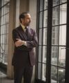 Deep burgundy wool suit with cream shirt, navy tie and white pocket square, worn by a model by tall windows