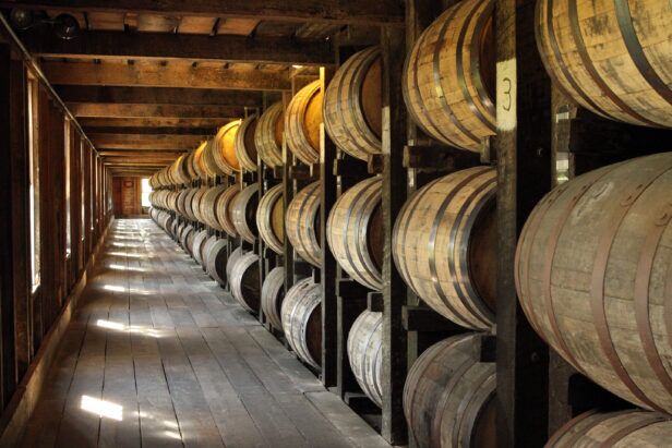 Oak bourbon barrels stacked on wooden racks in a sunlit rickhouse aisle, a lifestyle scene