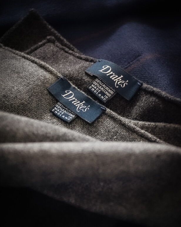 Grey cashmere pocket squares with woven brand labels, a close-up detail over navy cloth
