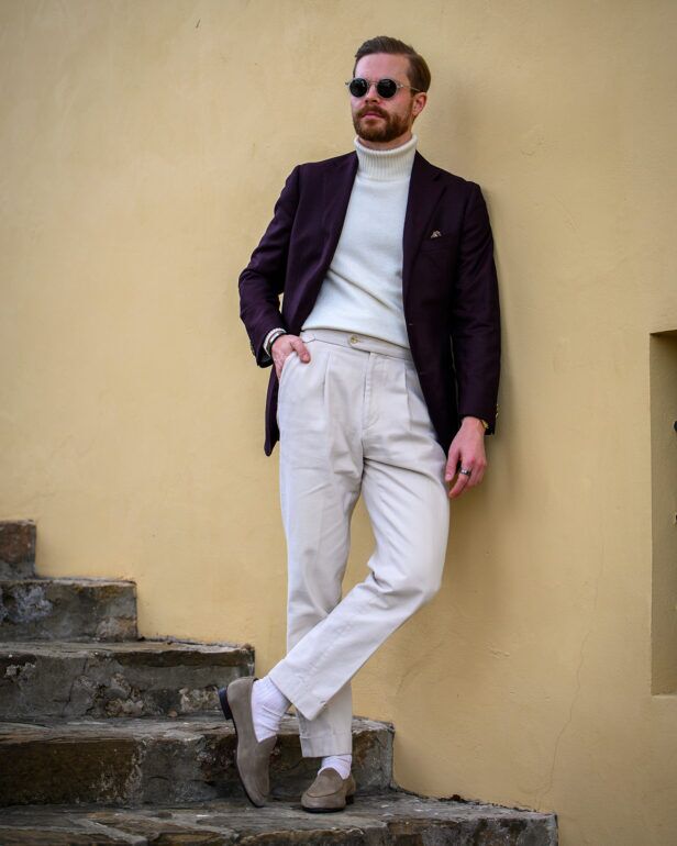 Deep aubergine wool sport coat with cream turtleneck and ivory pleated trousers, on stone steps