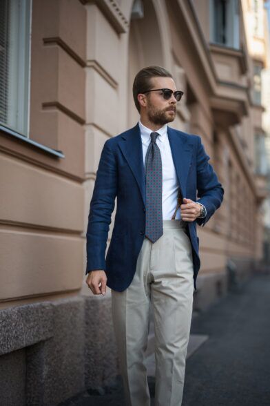 Navy linen sport coat with white shirt, teal medallion silk tie and cream pleated trousers, worn by a model on a city street