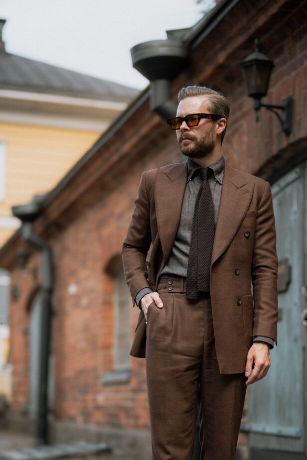 Brown double-breasted suit with grey shirt and brown knit tie, worn by a model on a brick street