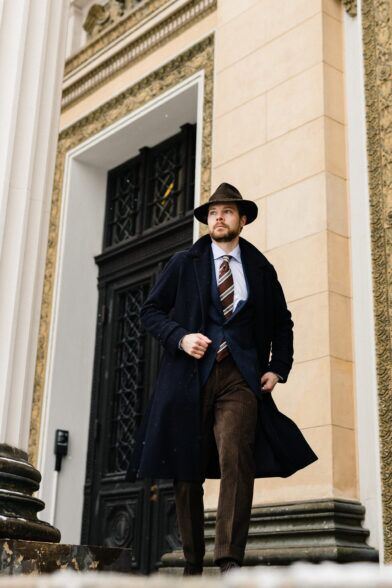 Navy wool overcoat with navy checked sport coat, striped tie and brown corduroy trousers, worn by a model on steps