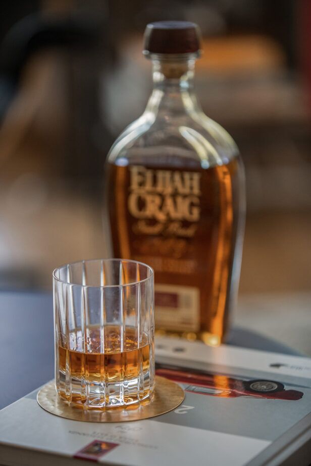Cut crystal tumbler of bourbon on a brass coaster beside an Elijah Craig bottle, a styled lifestyle scene