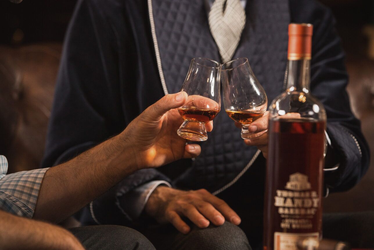 Navy quilted dressing gown with contrast piping over a cream shawl-collar cardigan, worn in a whiskey toast scene