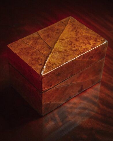 Tobacco leaf-wrapped keepsake box in warm brown, lid closed, in a dimly lit styled scene