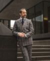 Grey plaid flannel double-breasted suit with light blue shirt, navy tie and white pocket square, worn by a model outdoors