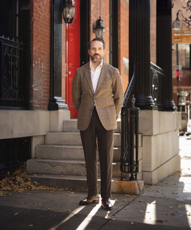 Brown glen plaid wool sport coat with white shirt, brown trousers and brown brogues, worn by a model on a city stoop
