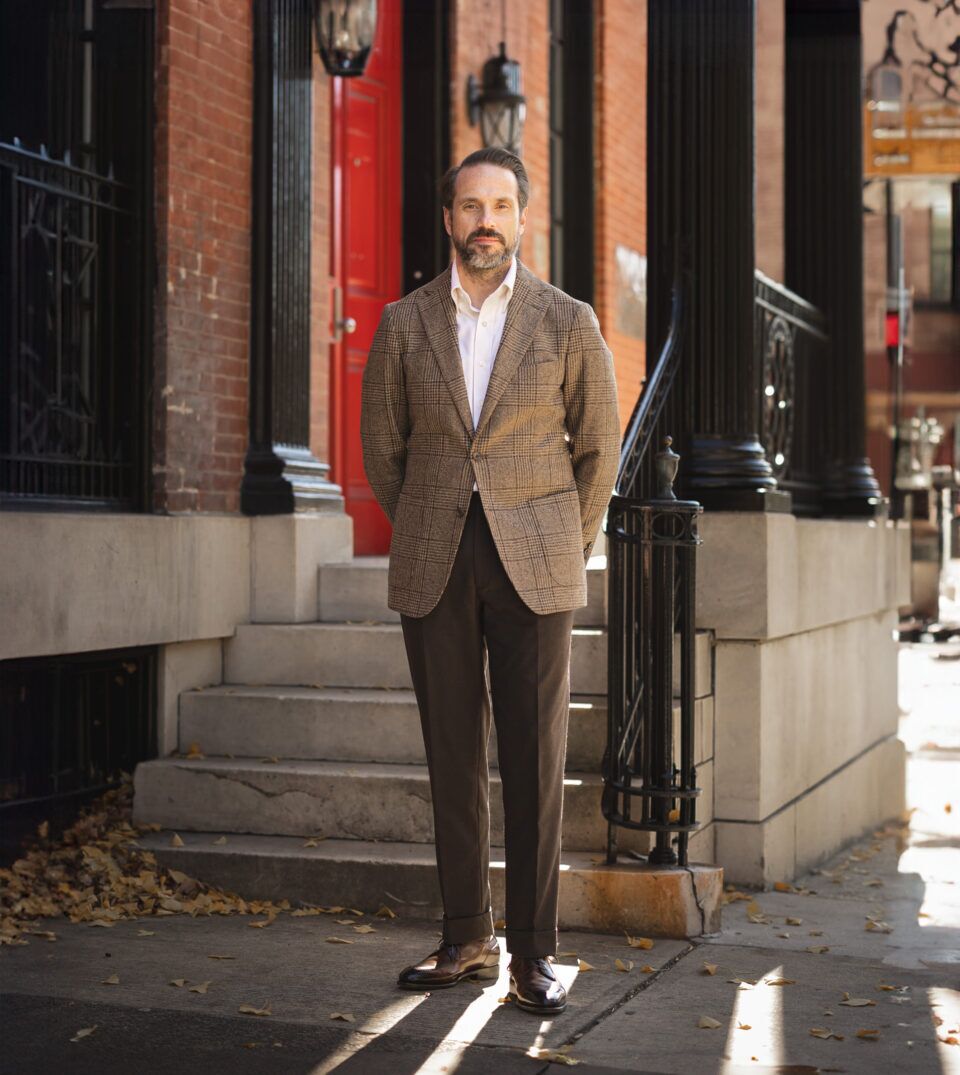 Brown glen plaid wool sport coat with white shirt, brown trousers and brown brogues, worn by a model on a city stoop