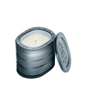 Refillable scented candle in an engraved metal travel tin, lit with lid propped alongside