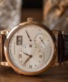 Rose gold dress watch with silver off-centre dial, big date and brown leather strap, close-up on wood