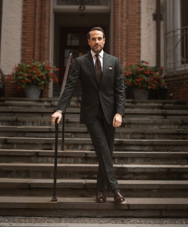 Dark green flannel two-button suit with white shirt, brown knit tie and brown oxfords, worn by a model on steps