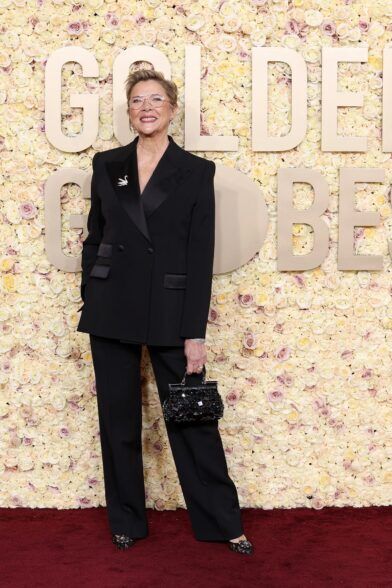 Black double-breasted tuxedo suit with satin peak lapels, swan brooch and beaded bag, on a red carpet