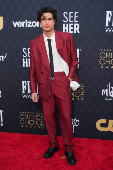 Deep red peak lapel suit with cream shirt, black tie and black loafers, worn on a red carpet