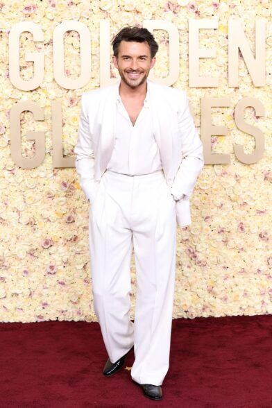 White shawl collar suit with open-neck white shirt and black patent shoes, worn on a red carpet