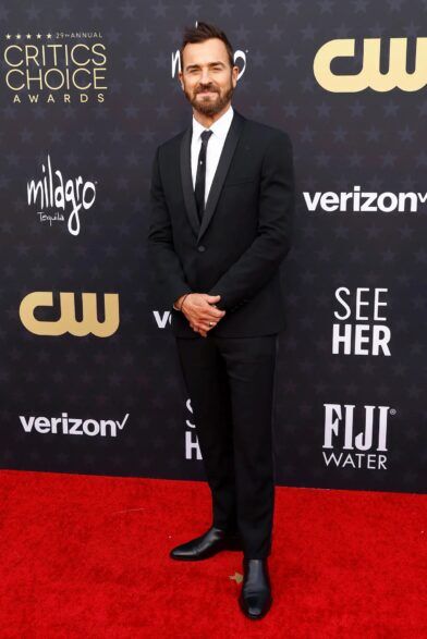 Black single-button dinner jacket with satin shawl lapel, white shirt, black tie and black boots, worn on a red carpet