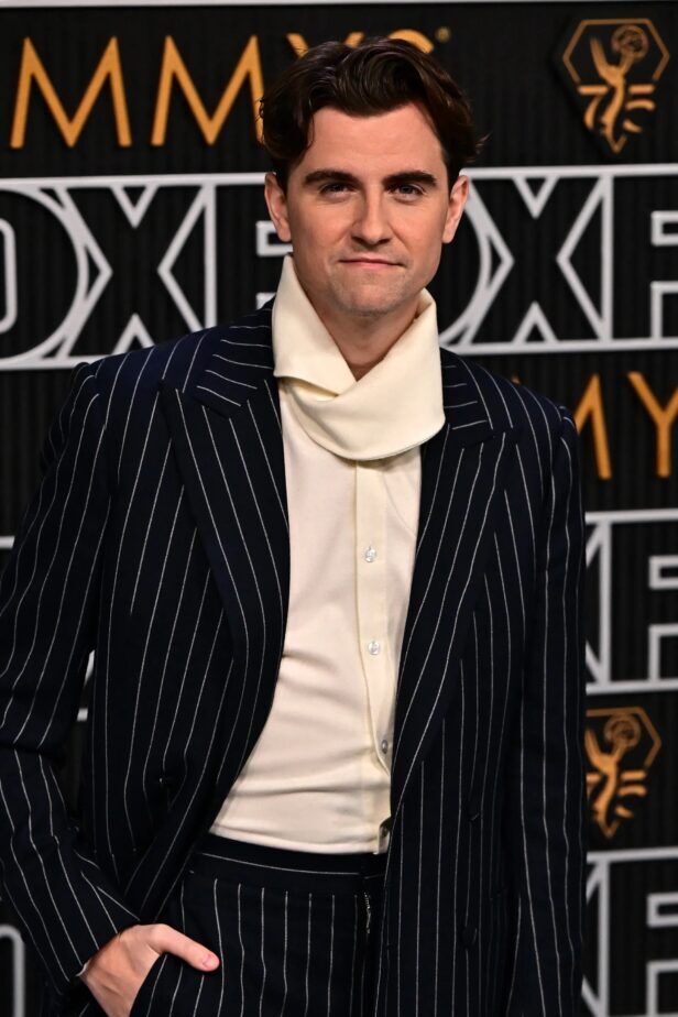 Navy chalk stripe suit with peak lapels and cream roll-neck knit shirt, worn by a man on a red carpet