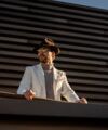 Cream corduroy sport coat with taupe turtleneck, brown felt fedora and sunglasses, worn by a model outdoors