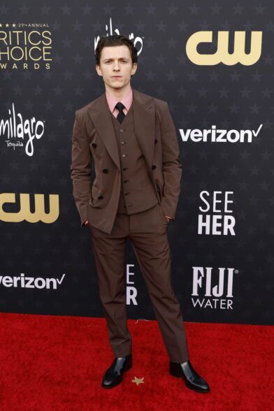 Brown three-piece double-breasted suit with pink shirt, black tie and black boots, worn on a red carpet