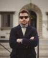 Navy textured wool double-breasted overcoat over a cream sweater and denim shirt, on a city street