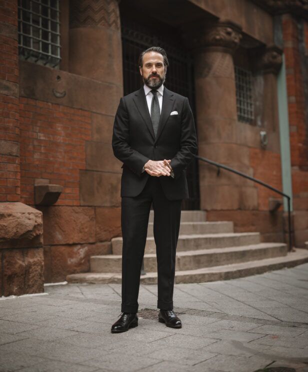 Black flannel suit with white shirt, grey tie, white pocket square and black oxfords, worn by a model on a city street