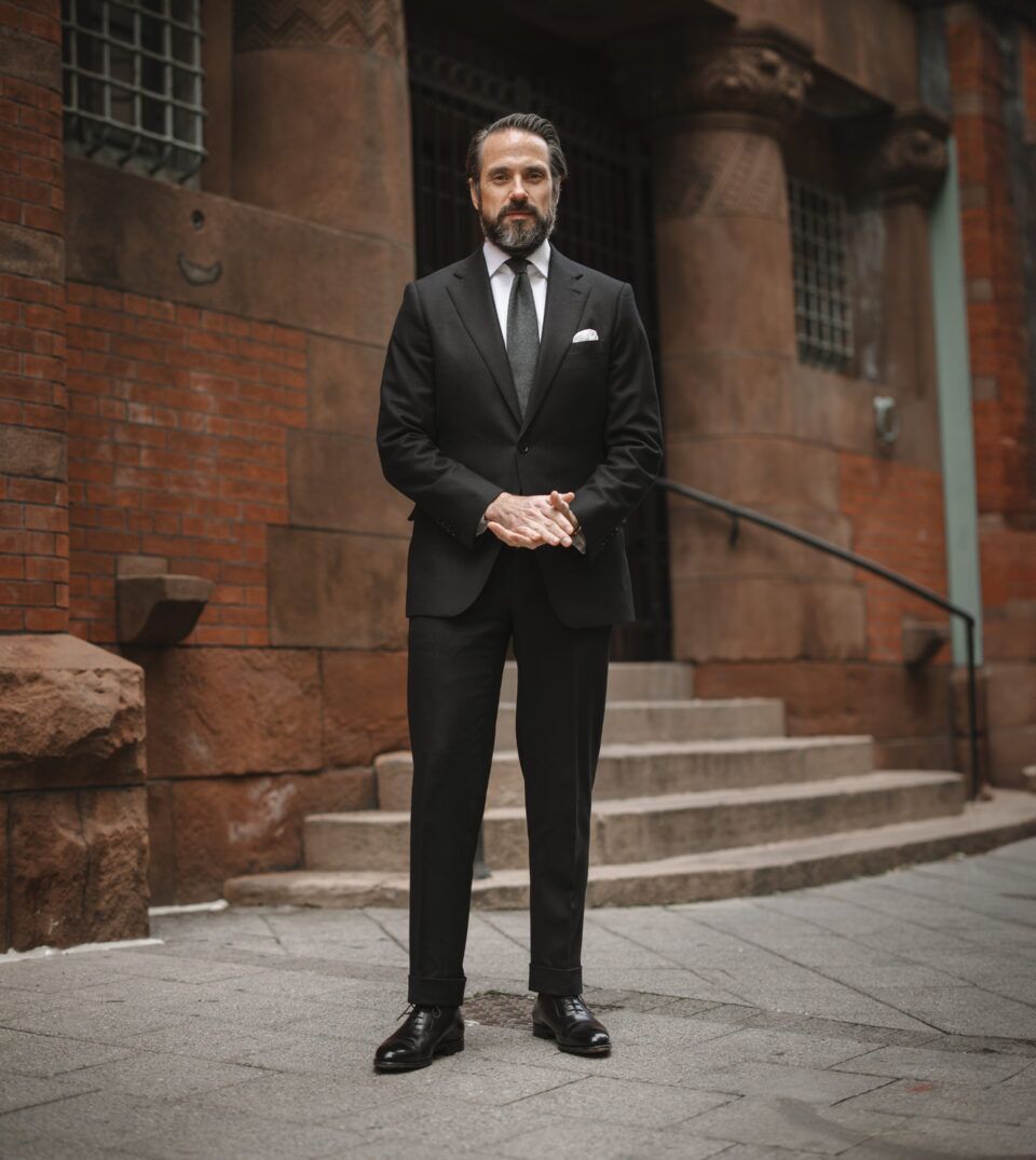 Black flannel suit with white shirt, grey tie, white pocket square and black oxfords, worn by a model on a city street