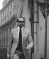 Light puppytooth three-piece suit with white shirt, dark knit tie and pocket square, worn by a model on a city street